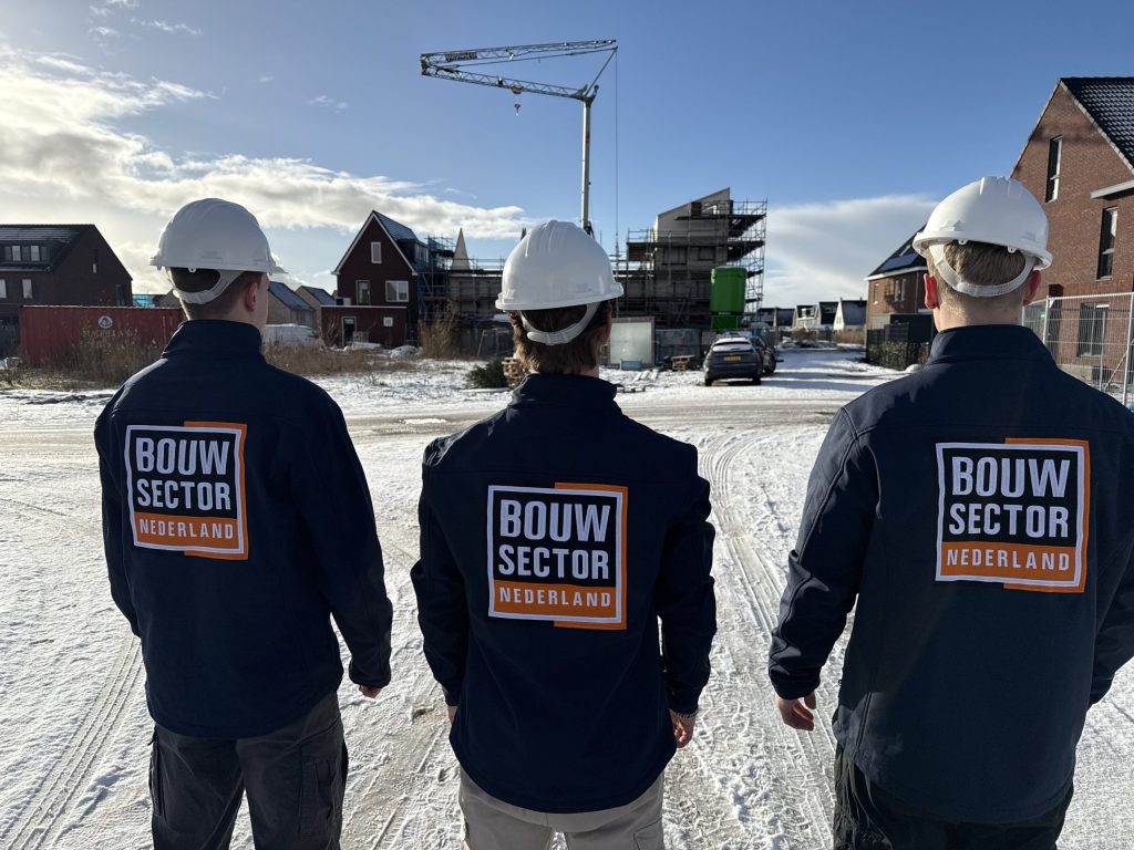 Drie vakmensen van Bouwsector Nederland met witte helm op een nieuwbouwlocatie in de sneeuw
